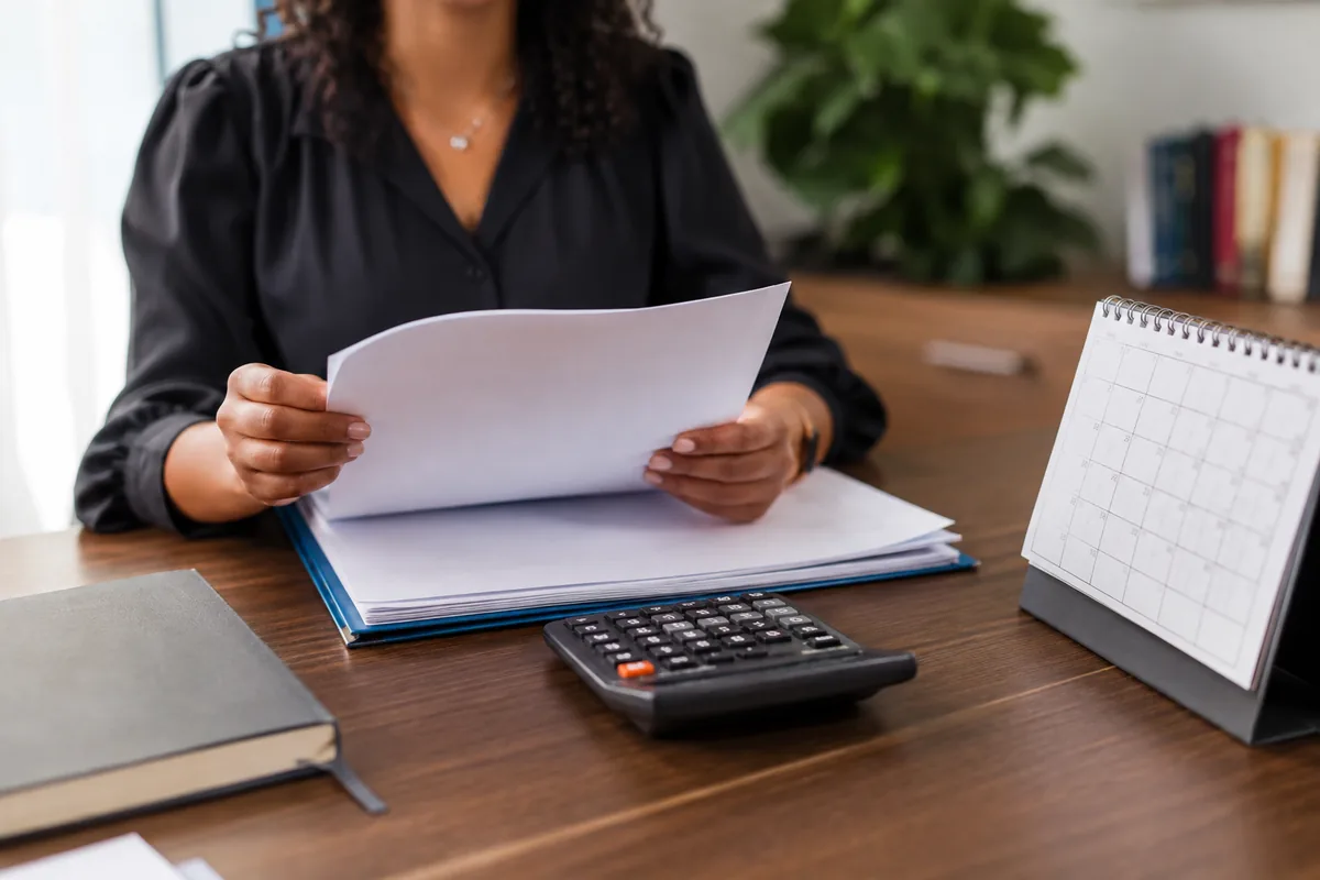Trabalhadora confere documentos de rescisão com calculadora e calendário