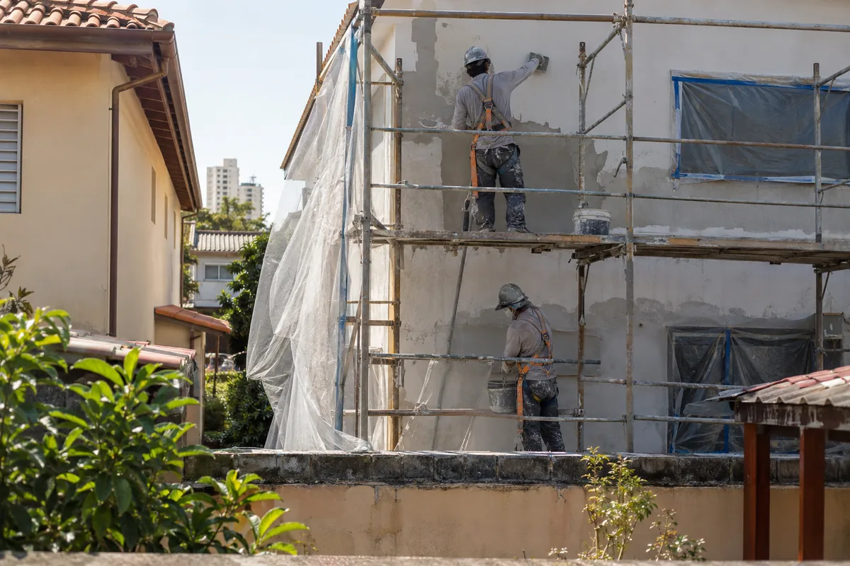 Obra residencial com andaime e proteção contra poeira junto ao imóvel vizinho